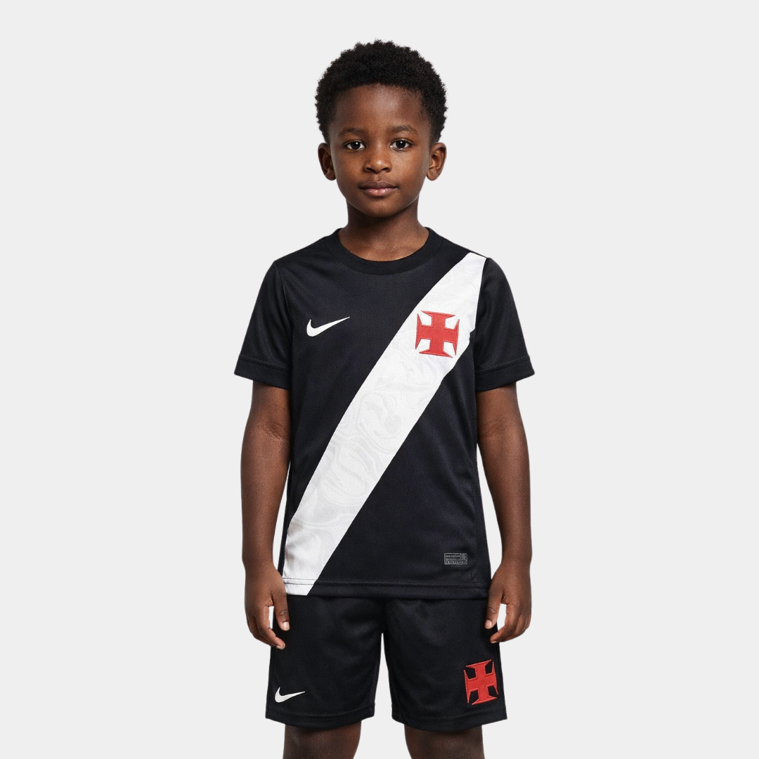 Vista frontal de um menino vestindo o kit infantil titular do Vasco da Gama na cor preta, com a icônica faixa diagonal branca atravessando o peito, ostentando a Cruz de Malta em vermelho e o logo da Nike em branco, acompanhado de calção preto com os mesmos emblemas.