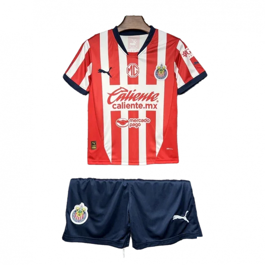 Kit infantil Chivas I 24/25 com camisa listrada vermelha e branca, shorts azul marinho, escudos e logos visíveis.
