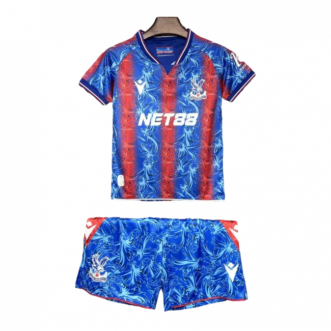 Kit infantil Crystal Palace 24/25 azul e vermelho com padrão exclusivo. Camisa e shorts com escudo e patrocínios. Fundo preto.