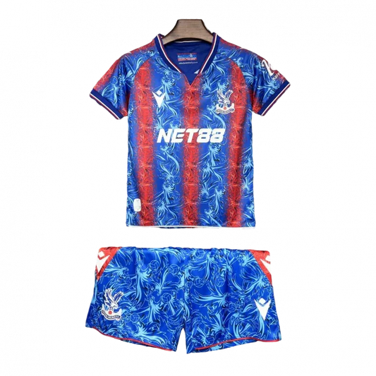 Kit infantil Crystal Palace 24/25 azul e vermelho com padrão exclusivo. Camisa e shorts com escudo e patrocínios. Fundo preto.