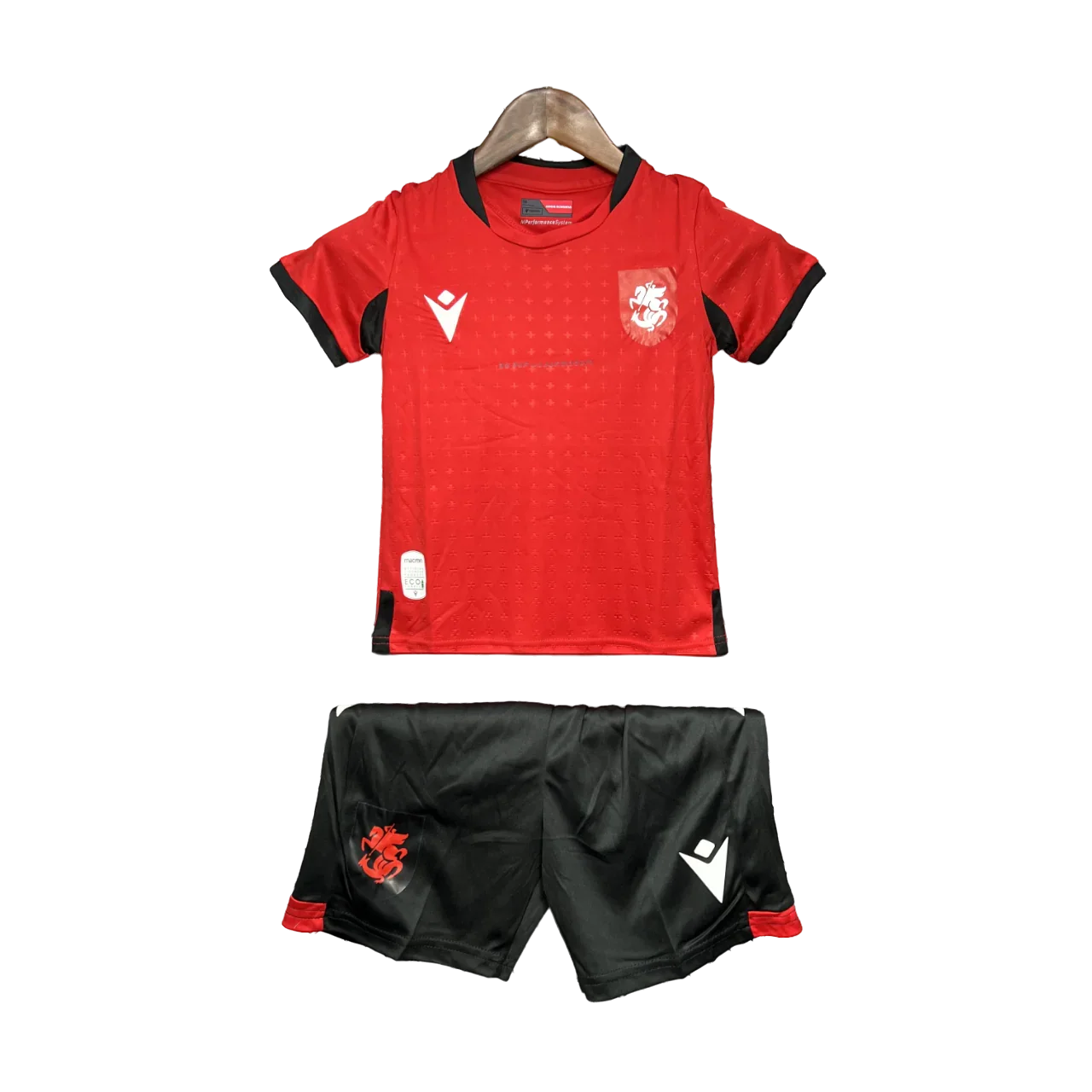Kit de futebol infantil da Georgia 24/25 com camisa vermelha e shorts pretos, exibido em cabide contra fundo preto.