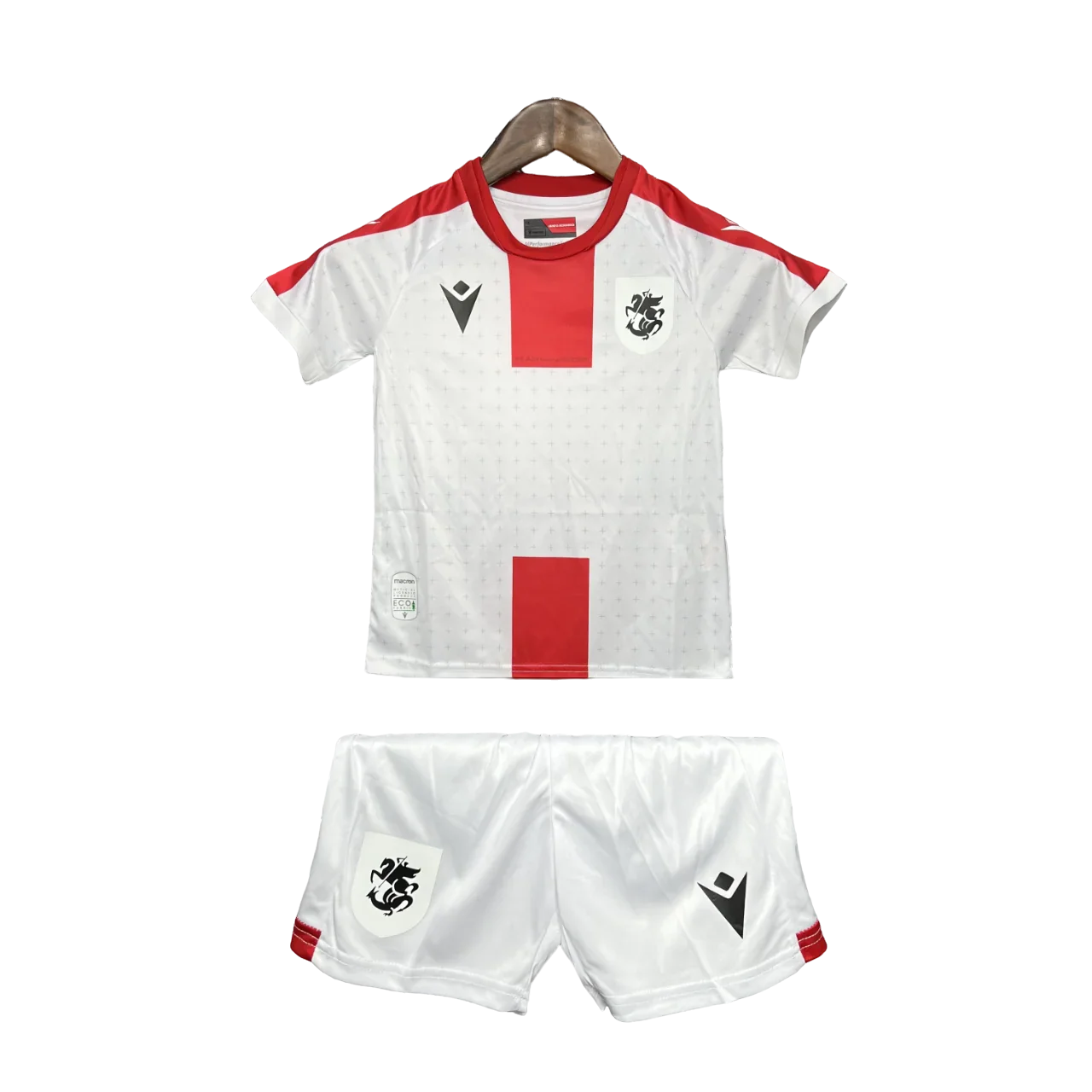Kit infantil Georgia 24/25, com camisa e shorts brancos. Camisa com faixas vermelhas, escudo preto e logo Macron preto. Shorts brancos com escudo e logo Macron pretos.