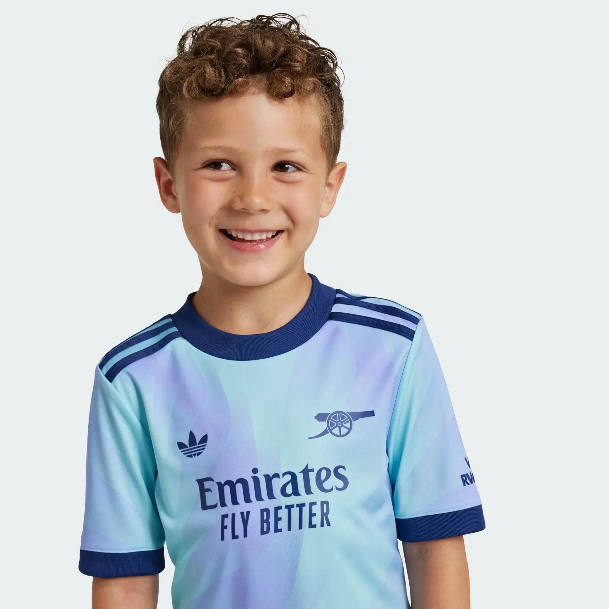 Camisa oficial infantil Arsenal 23/24, Kit Mini Mantos. Criança sorridente vestindo a camisa azul e roxa