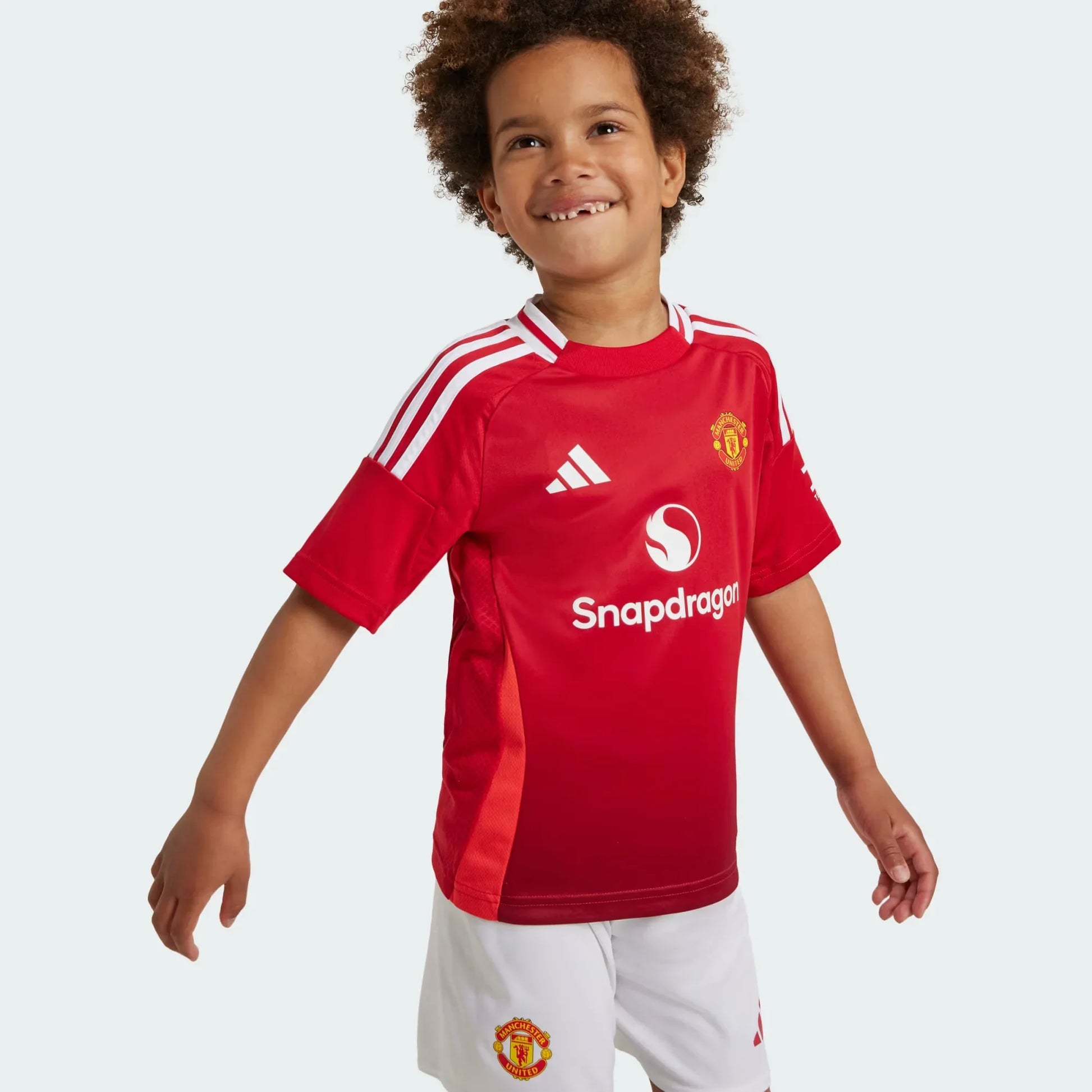 Mini Mantos infantil oficial kit camisa Manchester United, criança sorridente vestindo o uniforme de futebol do time