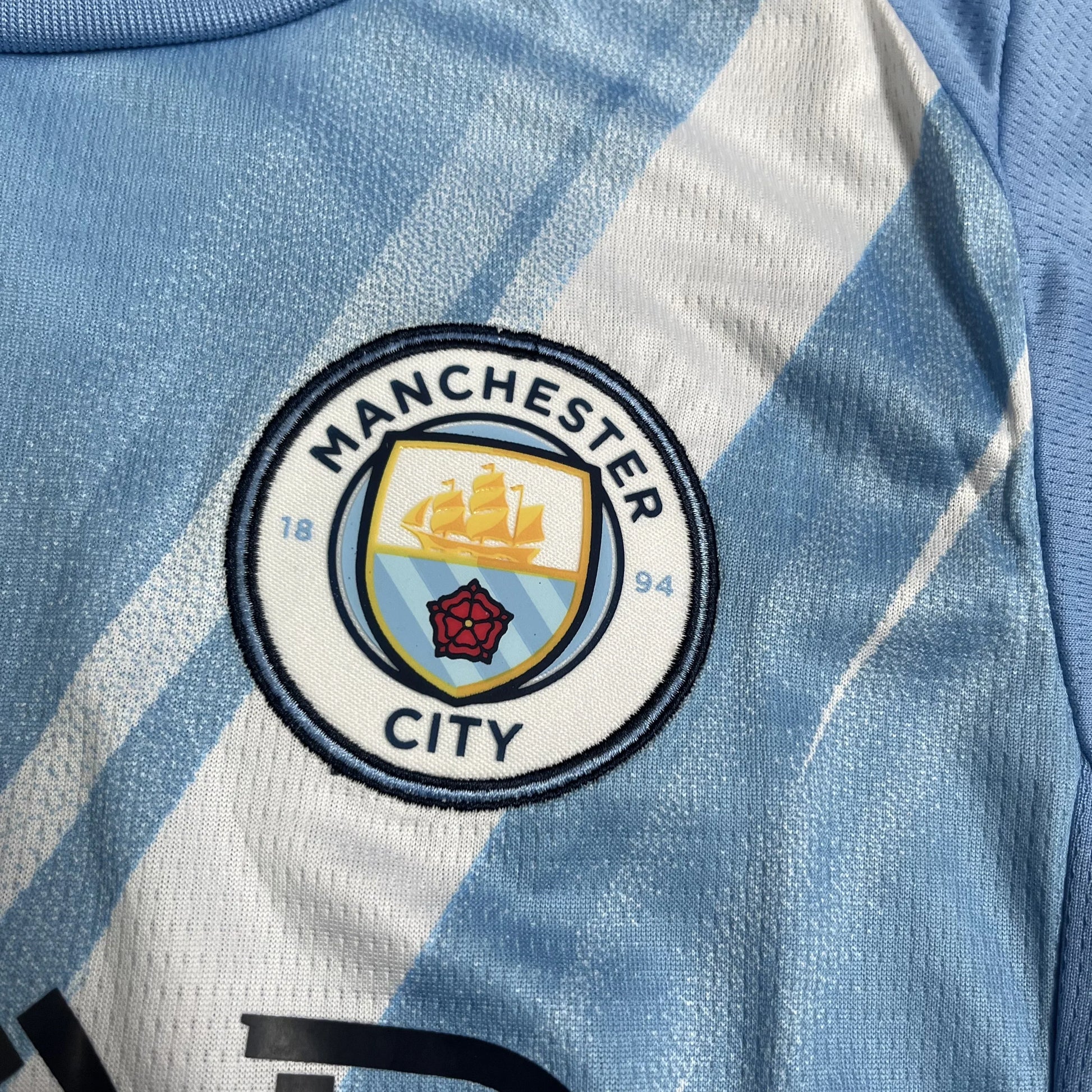 Mini Mantos: camisa oficial kit infantil Manchester City, detalhe do escudo