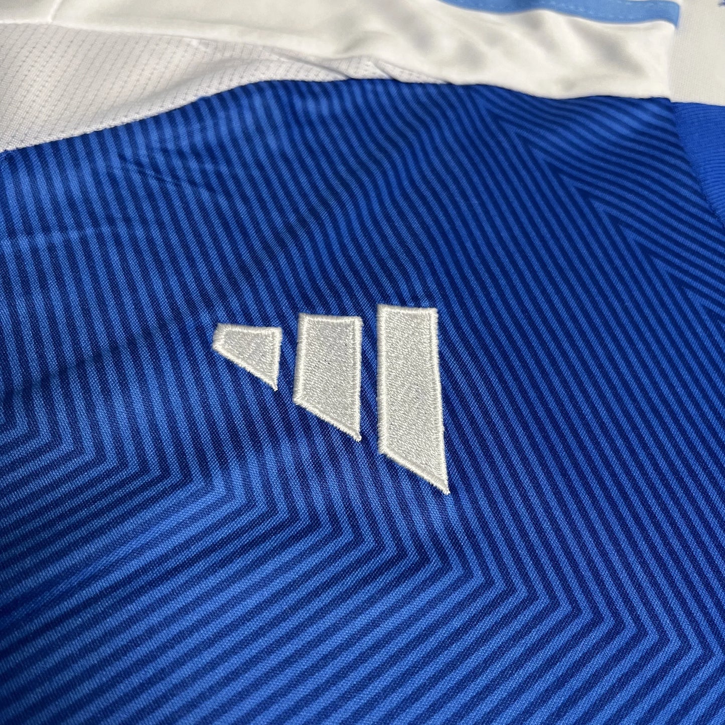 Camisa de futebol infantil azul com padrão listrado diagonal em tons de azul e detalhes brancos. Logo de três barras brancas bordado.