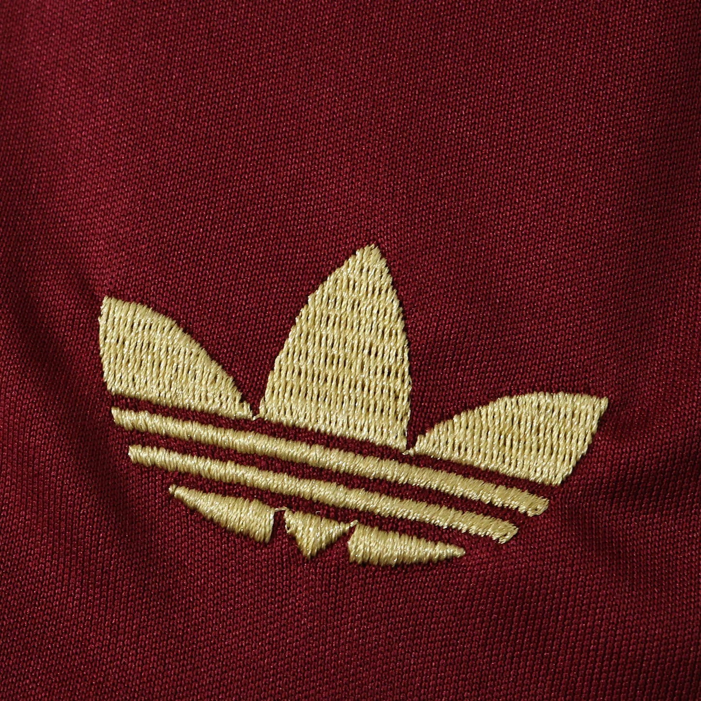 Logo Adidas Trefoil dourado bordado em tecido bordô.