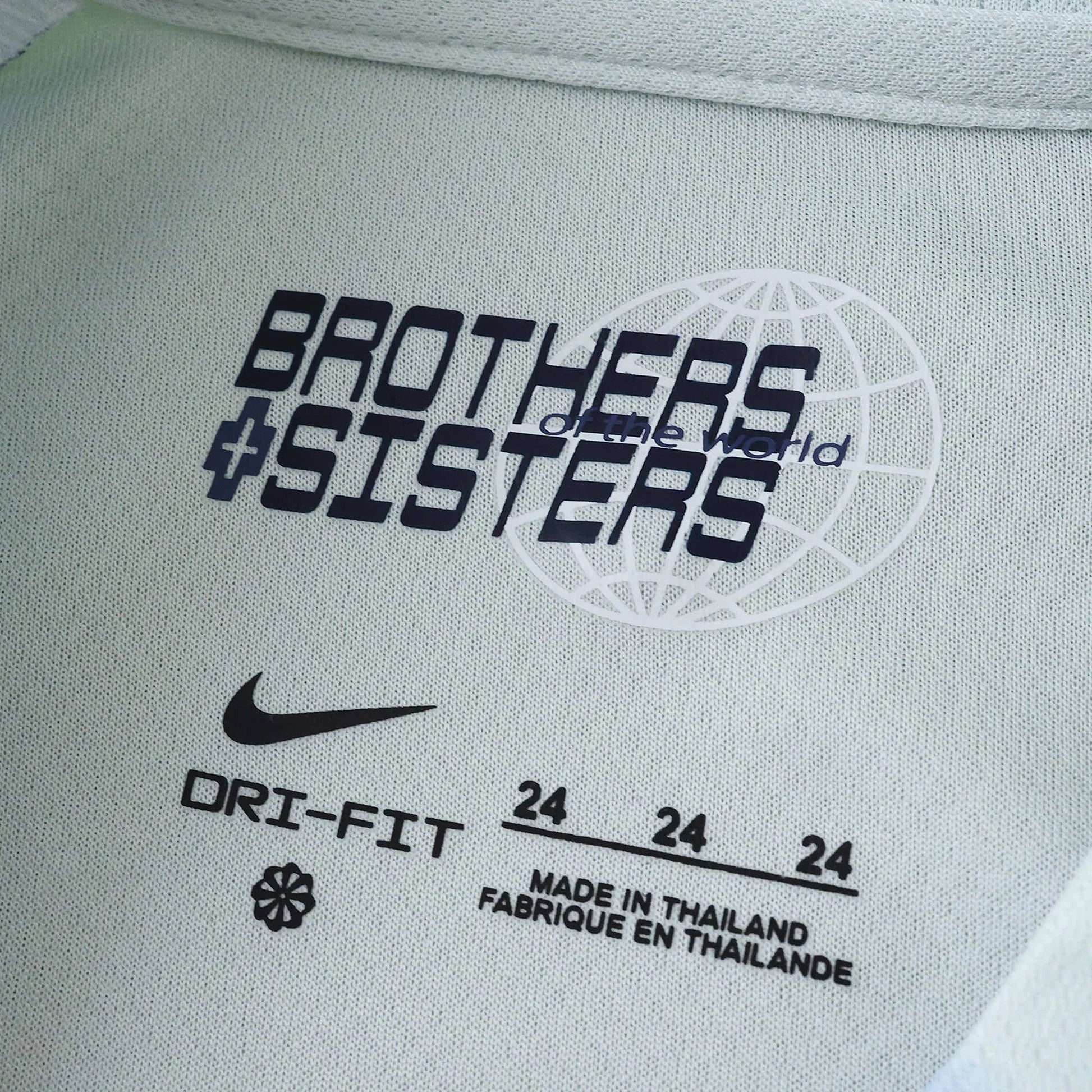 Detalhe da etiqueta interna em tecido verde-claro de camisa esportiva Nike Dri-Fit, com a frase 'Brothers & Sisters Of The World'.