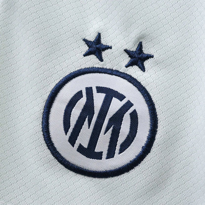 Close-up do distintivo bordado da Inter Milan em azul escuro e branco, com duas estrelas azuis, sobre um tecido azul claro.