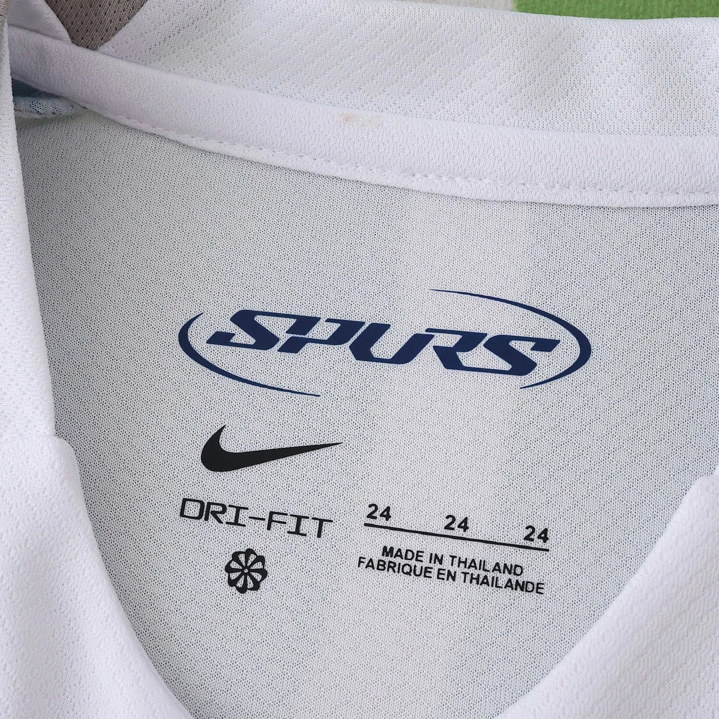 Close-up da etiqueta interna de uma camisa infantil branca do Spurs, mostrando o logo Nike, 'DRI-FIT' e 'MADE IN THAILAND'.