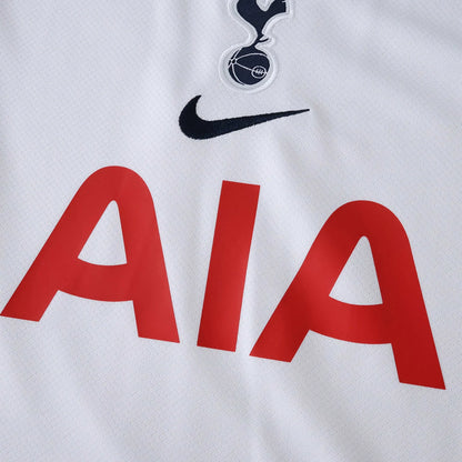 Camisa de futebol branca com escudo bordado de pássaro sobre bola, logo Nike preto e patrocínio 'AIA' em vermelho na frente. Detalhe da textura do tecido.