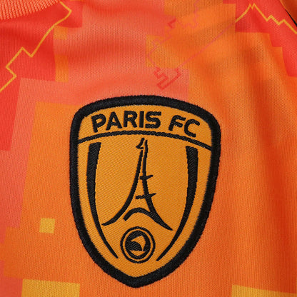 Camisa laranja Paris FC, detalhe do escudo bordado em preto com Torre Eiffel e fundo laranja claro.