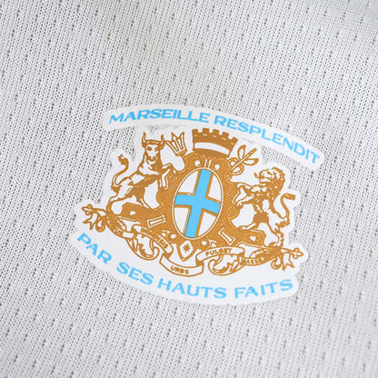 Camisa oficial infantil Marseille kit Mini Mantos: detalhe do escudo e tecido branco da camisa