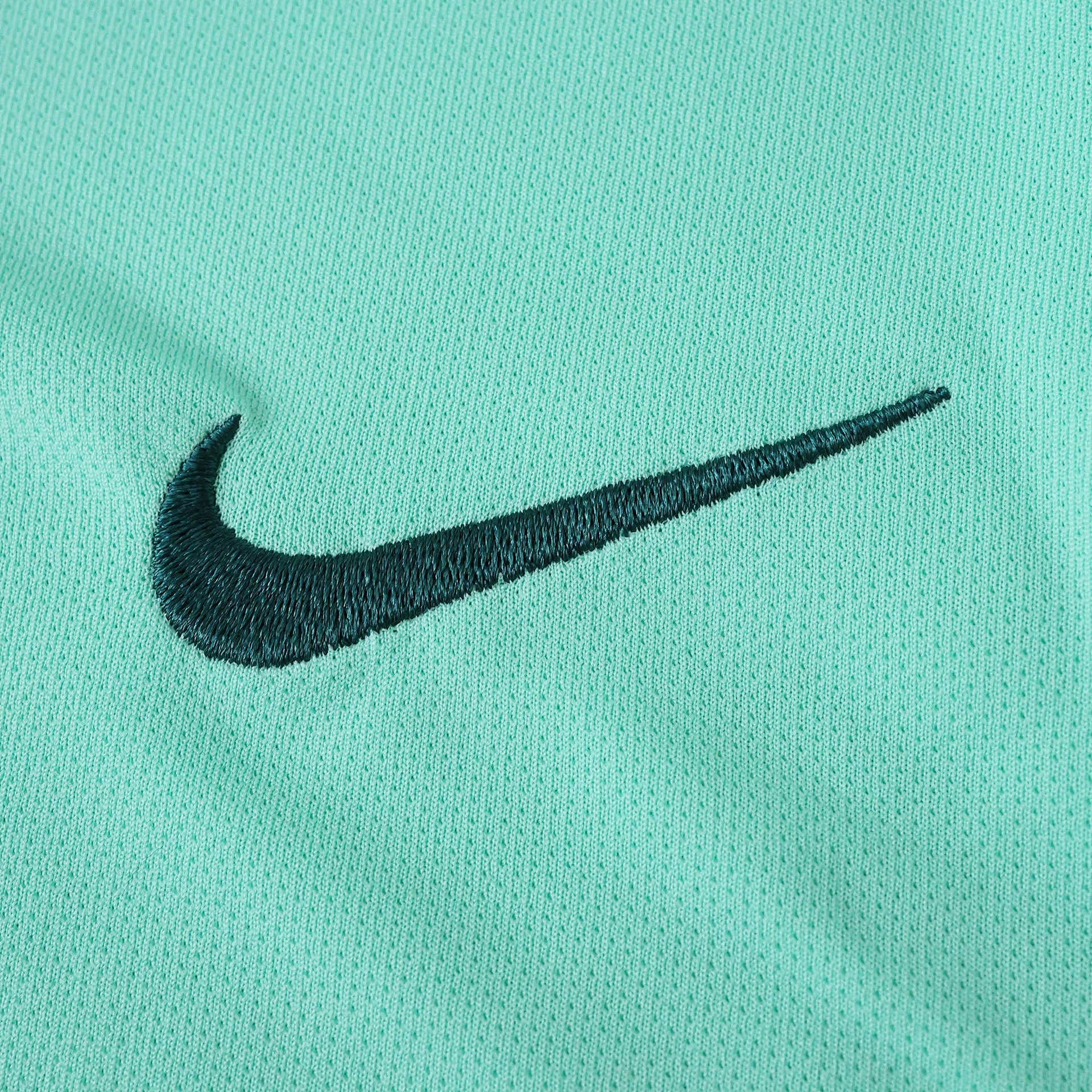 Detalhe da camisa verde-água com logo Nike bordado em verde-escuro, mostrando a textura do tecido respirável.
