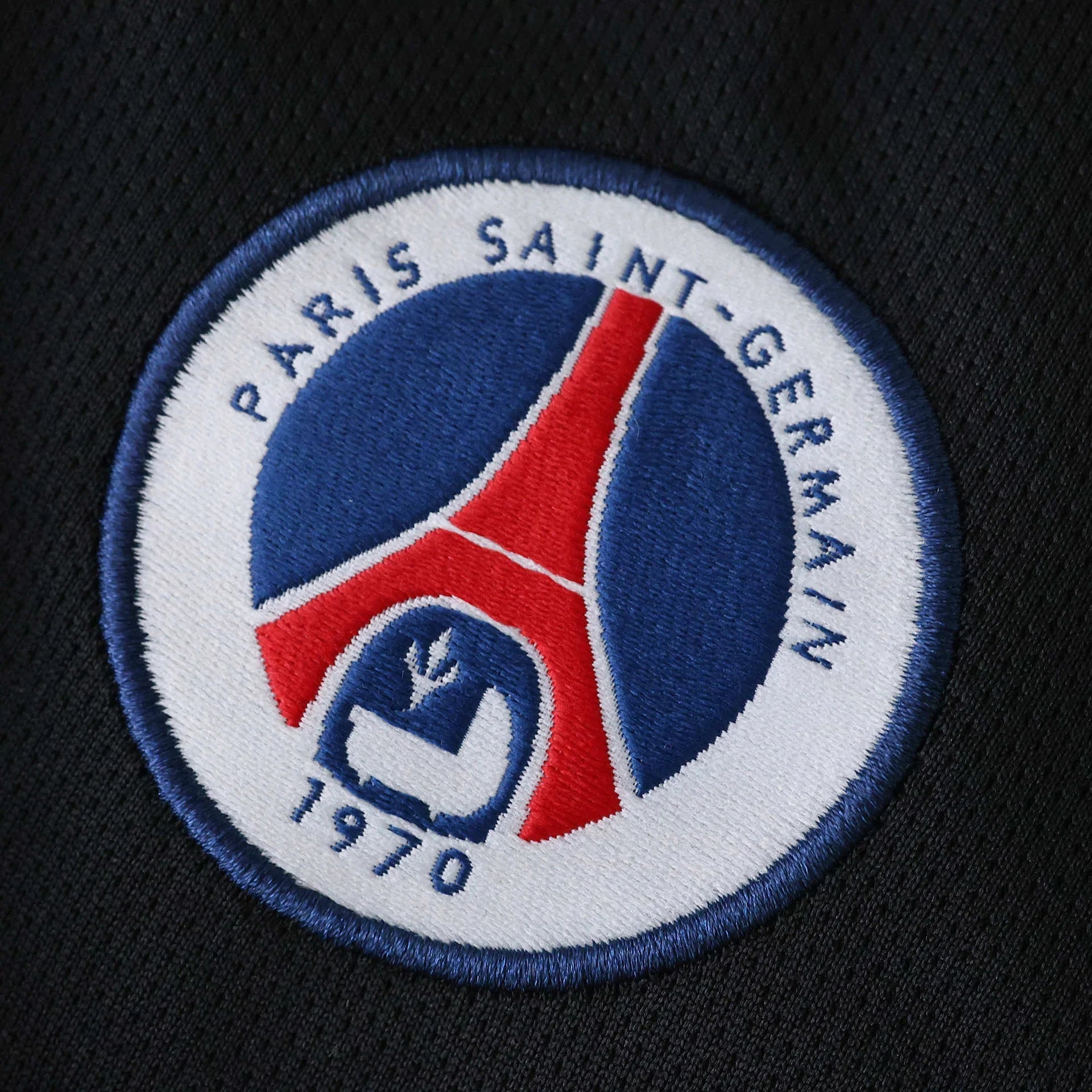 Escudo bordado do Paris Saint-Germain em tecido escuro. Emblema circular branco, azul e vermelho com Torre Eiffel e ano 1970.