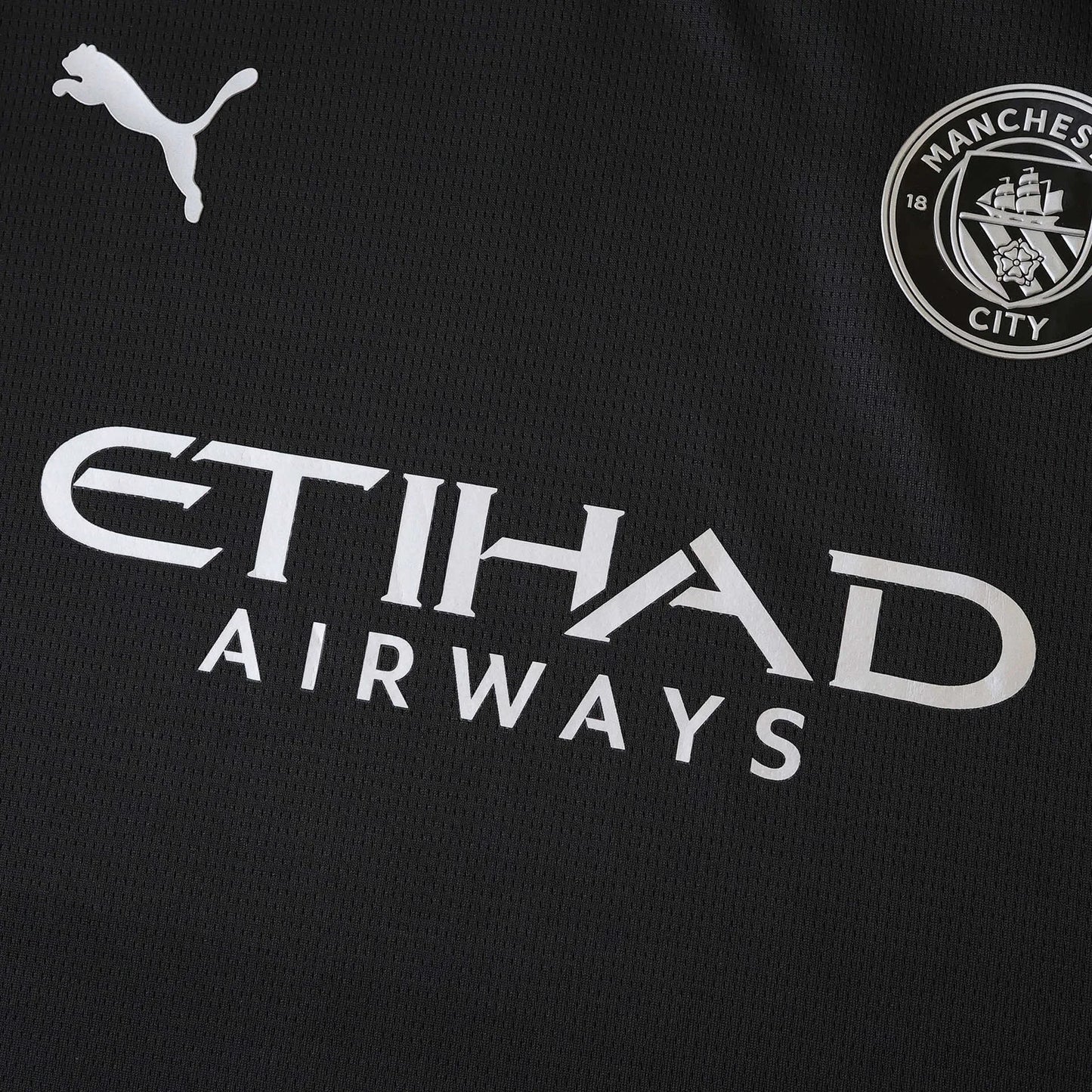 Camisa de futebol preta do Manchester City com logos da Puma, Etihad Airways e o escudo do clube em branco/prata.