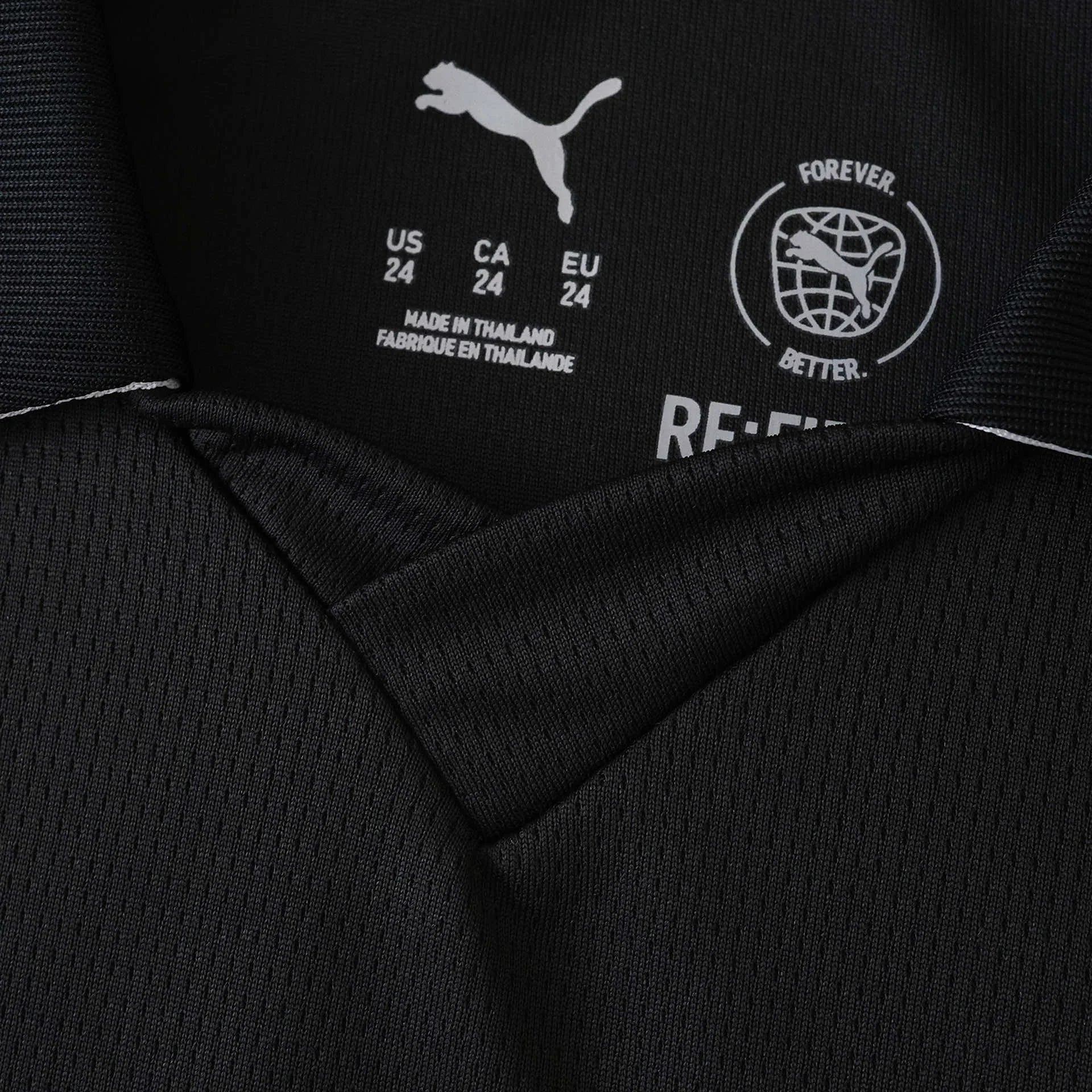 Foto em close da etiqueta interna de uma camisa preta Puma. Mostra o logo Puma, tamanhos (US/CA/EU 24) e 'MADE IN THAILAND'.