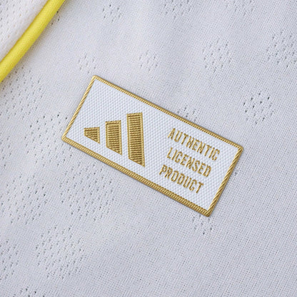 Close-up da camisa branca de futebol com um selo retangular branco e dourado escrito 'Authentic Licensed Product'.