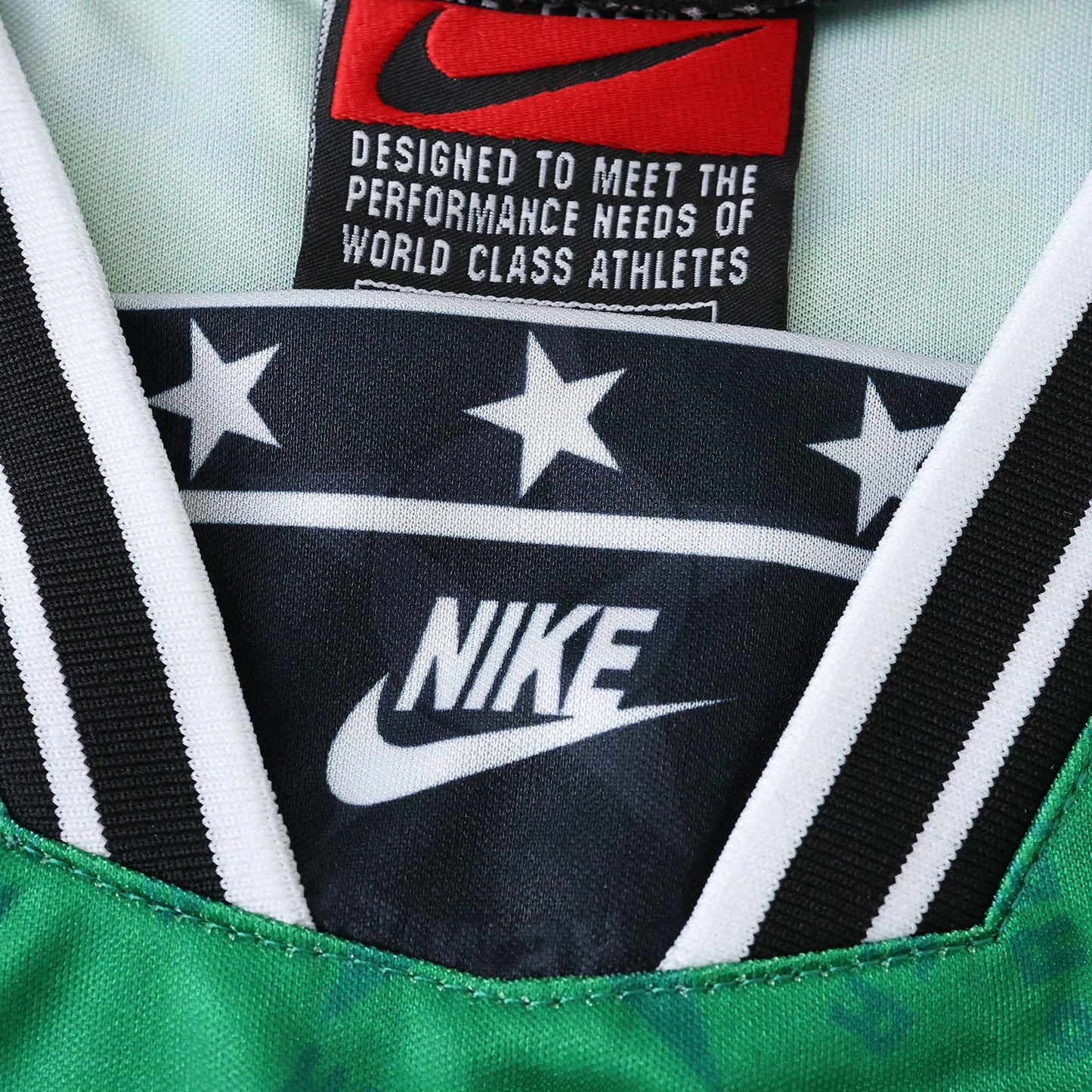 Camisa infantil oficial Nigeria Mini Mantos. Detalhe do kit verde Nike com estrelas na gola e tag