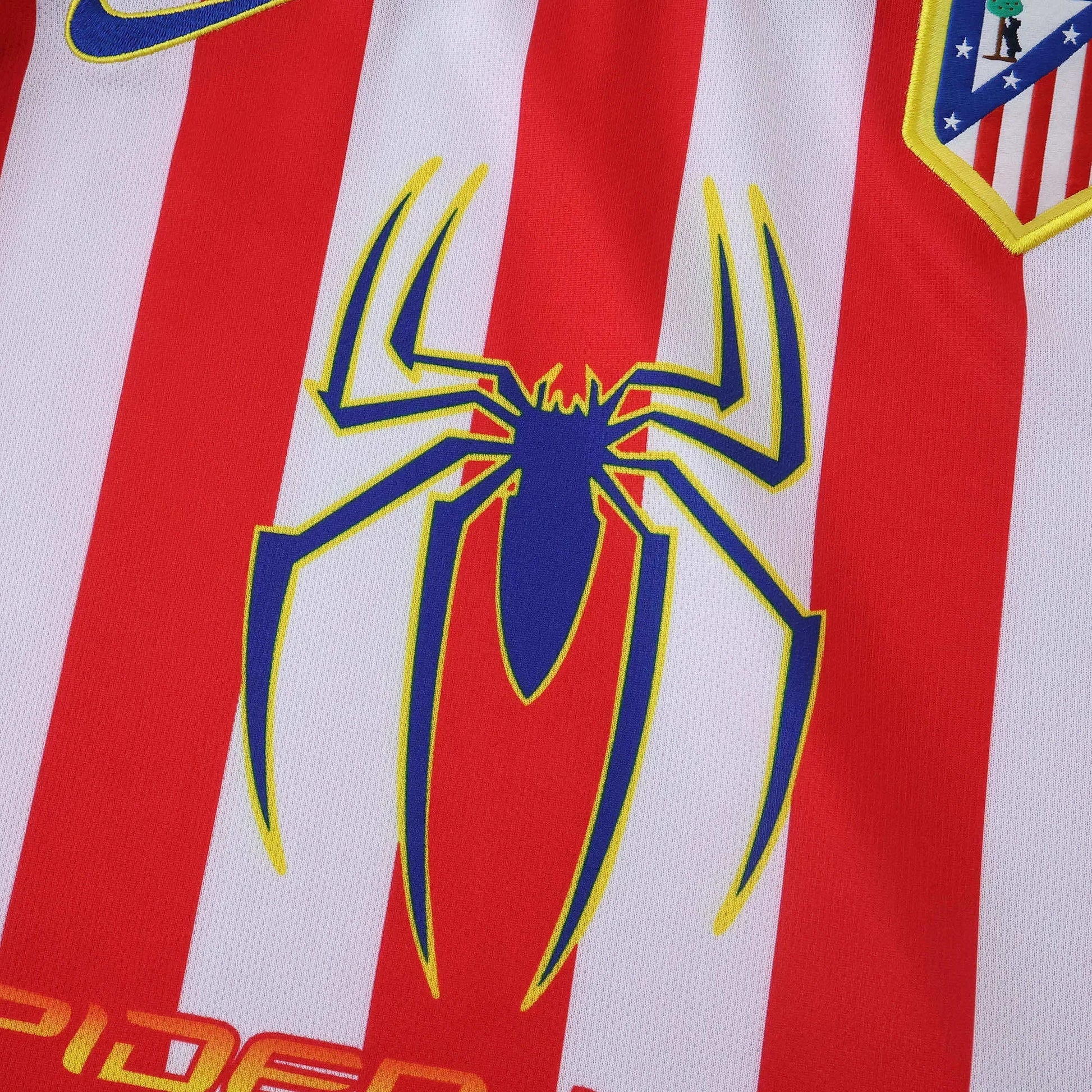 Camisa infantil listrada em vermelho e branco com logo azul de aranha amarela. Escudo do Atlético de Madrid e logo Nike visíveis.