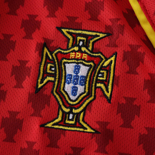 Close-up da camisa de futebol vermelha de Portugal. Escudo bordado da FPF em vermelho, amarelo, preto e azul com padrão da Cruz de Cristo.