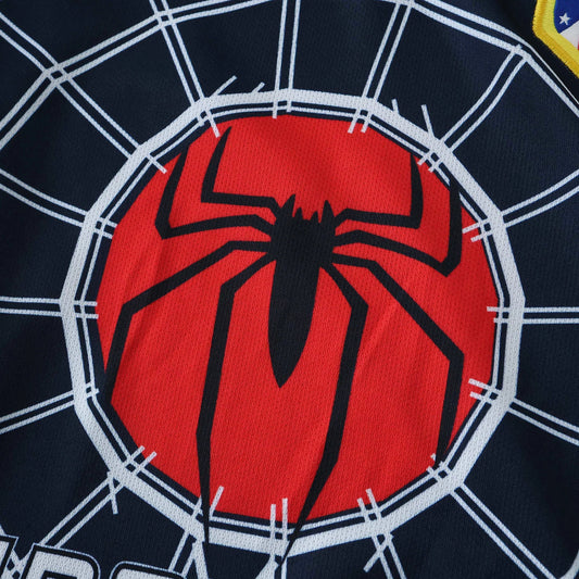 Close-up de camisa infantil azul escura com teia de aranha branca, logo do Homem-Aranha em círculo vermelho e patch amarelo.