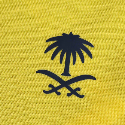 Close-up de tecido amarelo vibrante com um emblema em relevo azul-escuro, mostrando uma palmeira acima de dois sabres cruzados.