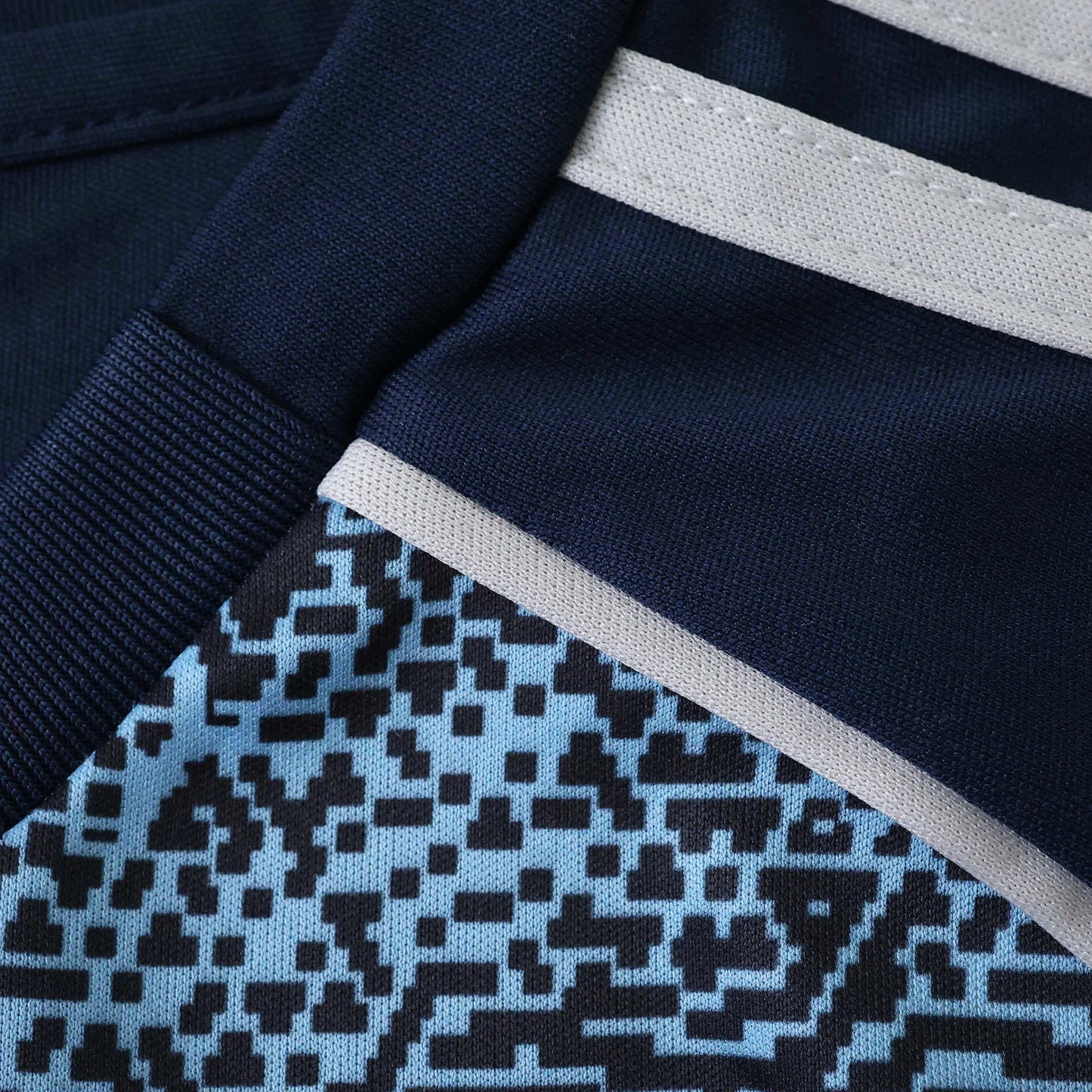 Close-up de kit de futebol infantil azul marinho com listras cinza claro e padrão pixelado em azul e preto.