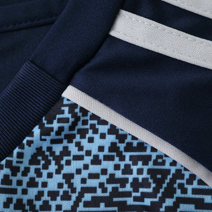 Close-up de kit de futebol infantil azul marinho com listras cinza claro e padrão pixelado em azul e preto.