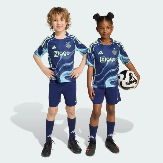 Duas crianças sorridentes vestindo o kit infantil do Ajax II em azul marinho com detalhes verde-limão. A menina segura uma bola de futebol.
