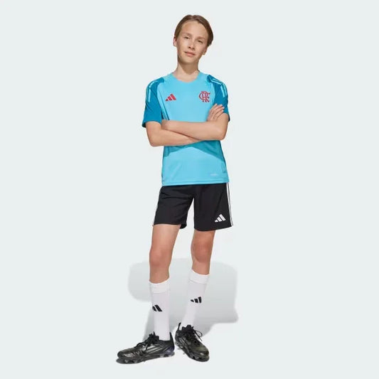 Menino em pé usando camisa de treino azul-claro com escudo do Mengão em vermelho, shorts pretos, meias brancas e chuteiras.