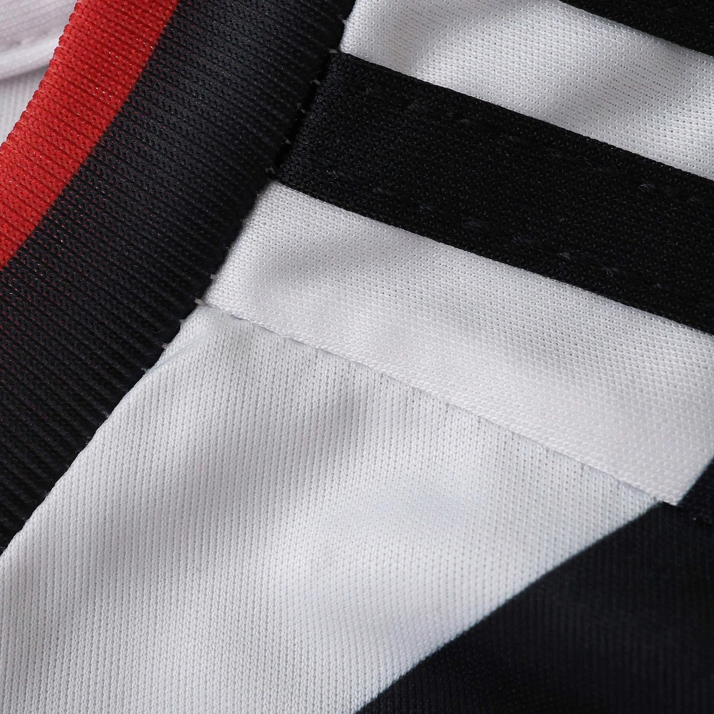 Close-up de tecido branco com listras pretas diagonais, e faixa vermelha e preta na borda superior. Textura do tecido visível.