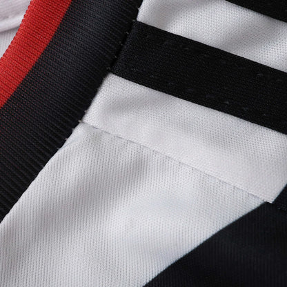 Close-up de tecido branco com listras pretas diagonais, e faixa vermelha e preta na borda superior. Textura do tecido visível.