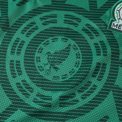 Camisa de futebol infantil do México verde escura com padrão circular sutil do calendário asteca e brasão parcial da seleção.