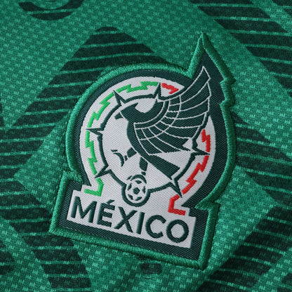 Escudo bordado da seleção do México em camisa verde escura com padrão. Águia, bola de futebol, cores verde, branco e vermelho.