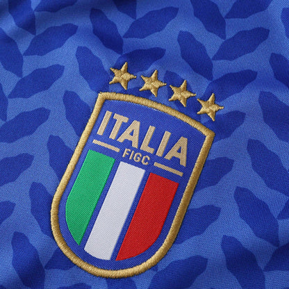 Detalhe do escudo da Itália com quatro estrelas douradas sobre uma camisa azul texturizada.