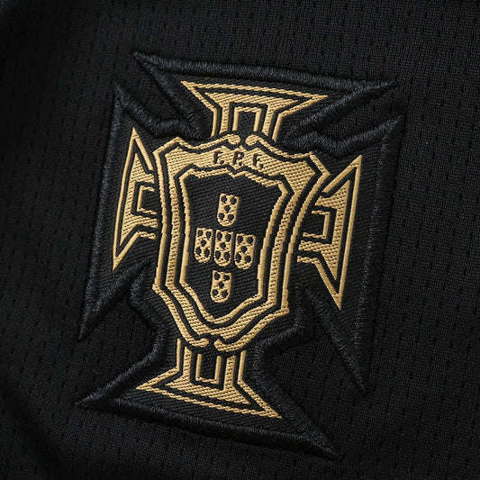 Emblema bordado da seleção de Portugal em dourado sobre tecido preto de malha, exibindo a Cruz de Cristo e escudo com FPF.