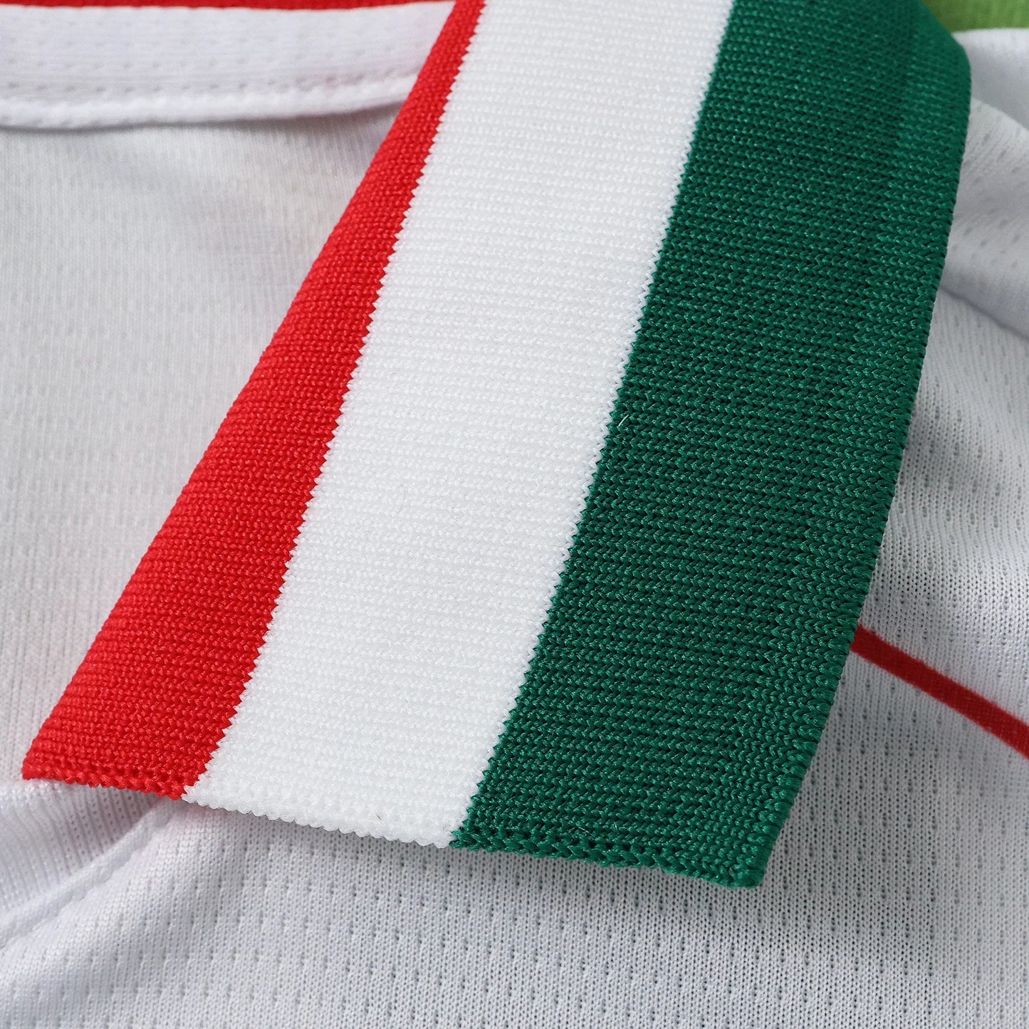 Detalhe do colarinho de camisa infantil branca com faixa tricolor (vermelho, branco, verde).