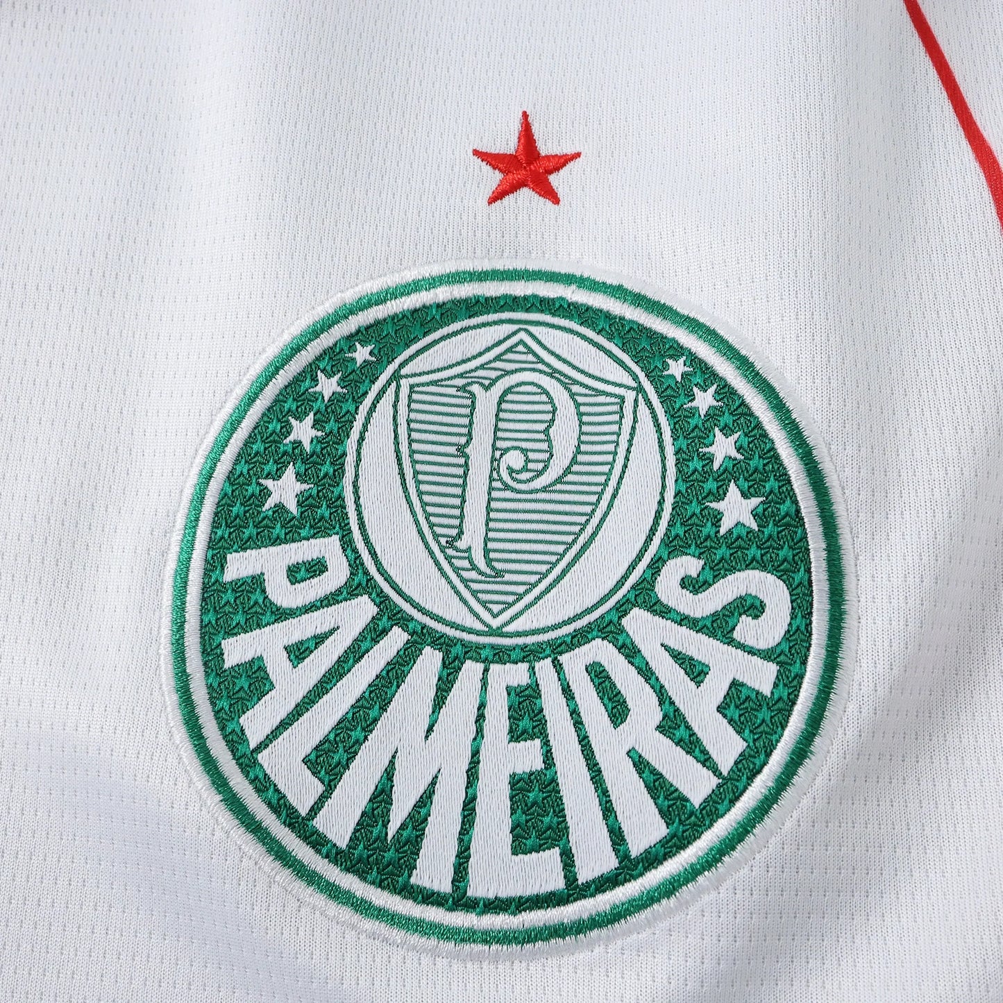 Escudo bordado do Palmeiras em camisa branca, com detalhe de estrela vermelha acima. Escudo verde e branco com o nome PALMEIRAS e a letra P centralizada.