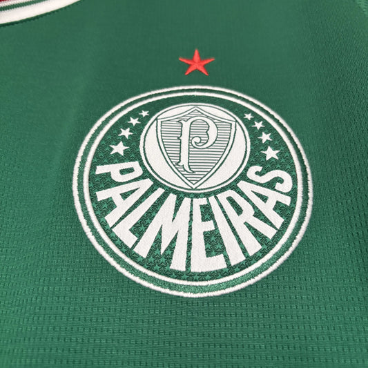 Close detalhado do escudo oficial do Palmeiras bordado em branco sobre o tecido verde da camisa, apresentando a estrela vermelha acima do emblema.