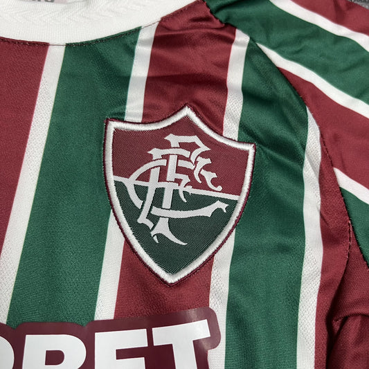 Close detalhado do escudo clássico do Fluminense Football Club aplicado sobre as listras tricolores da camisa.