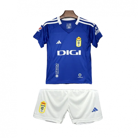 Kit infantil Oviedo I 24/25 completo em fundo preto. Camisa azul com escudo do Oviedo, logo Adidas, patrocínio DIGI e shorts brancos.