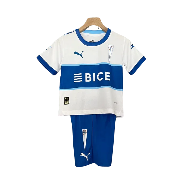 Kit infantil Universidad Católica I 24/25. Camisa branca com faixas azuis, shorts azuis. Escudos, logos Puma e patrocinadores BICE.